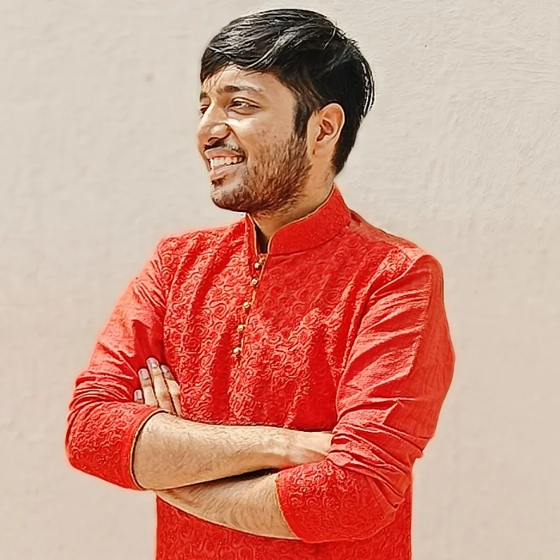 Arnab Mathur in a red kurta, arms crossed, smiling against a plain wall